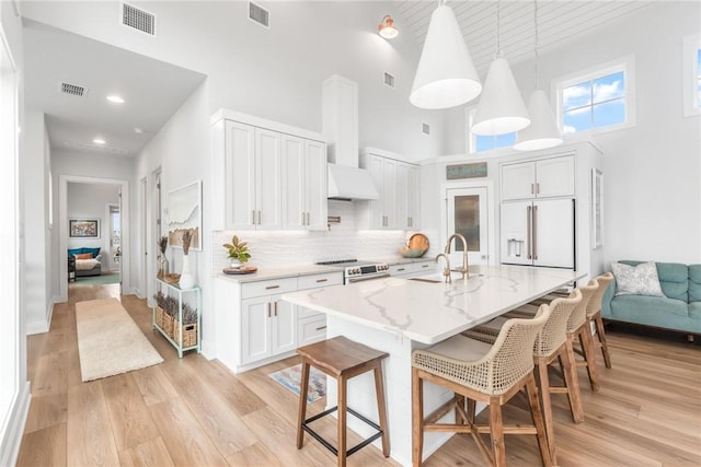 kitchen featuring a breakfast bar, visible vents, a sink, white built in refrigerator, and light wood-type flooring