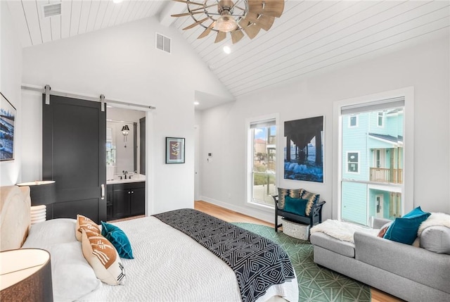 bedroom with a barn door, ensuite bath, wood finished floors, and visible vents