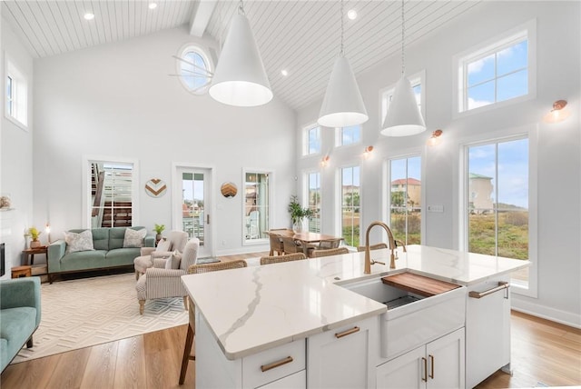 kitchen with light stone counters, open floor plan, decorative light fixtures, light wood-type flooring, and a sink