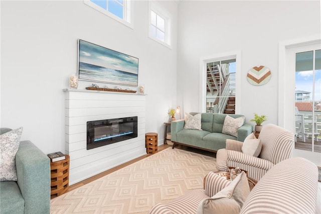 living room featuring a glass covered fireplace, stairway, a towering ceiling, and wood finished floors