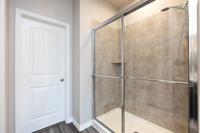 bathroom with baseboards, wood finished floors, and a shower stall