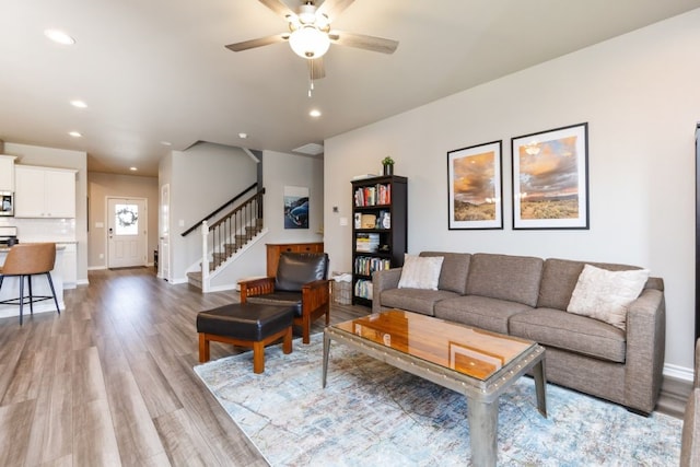 living area featuring a ceiling fan, baseboards, light wood-style flooring, recessed lighting, and stairs