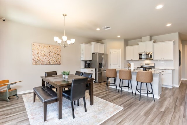 dining area featuring light wood-style flooring, baseboards, visible vents, and a chandelier