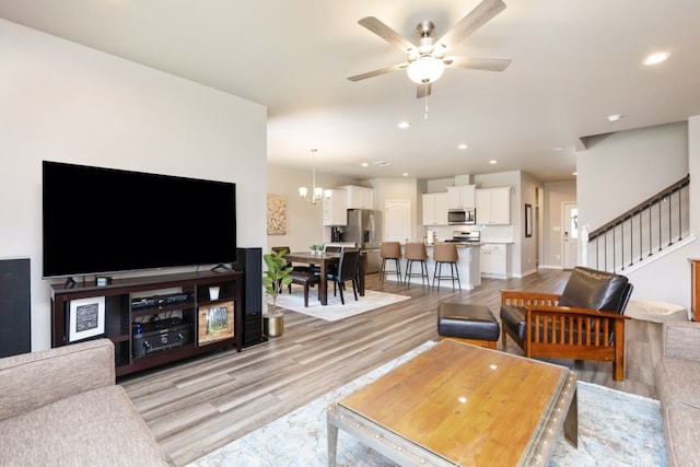 living room with recessed lighting, stairway, light wood-style floors, and ceiling fan with notable chandelier