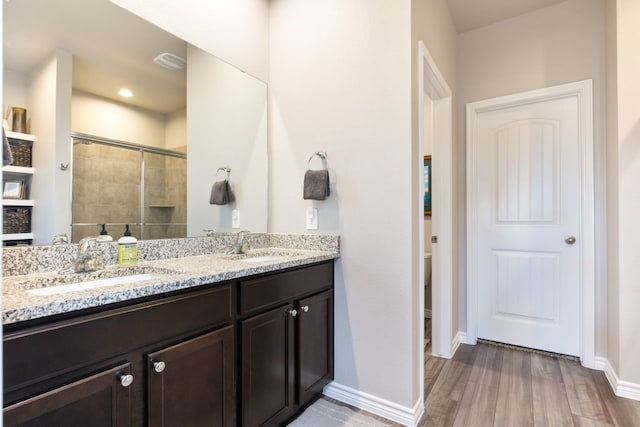 full bathroom featuring double vanity, tiled shower, wood finished floors, and a sink