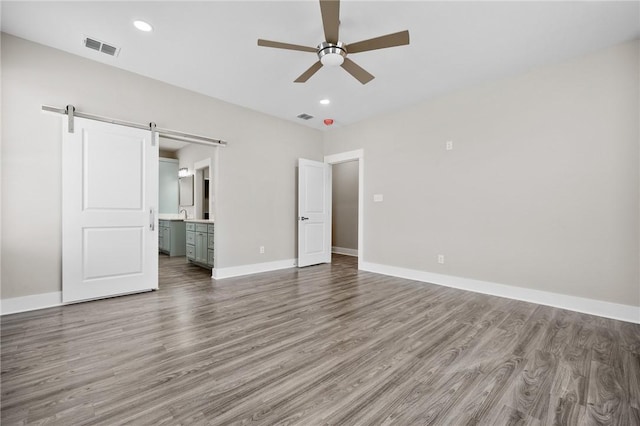 unfurnished bedroom featuring a barn door, hardwood / wood-style flooring, ceiling fan, and connected bathroom