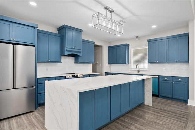 kitchen with light stone countertops, stainless steel appliances, hardwood / wood-style floors, decorative light fixtures, and a kitchen island