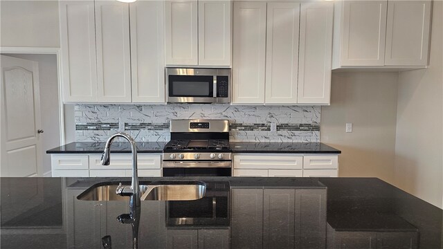 kitchen featuring stainless steel appliances, white cabinetry, and dark stone counters