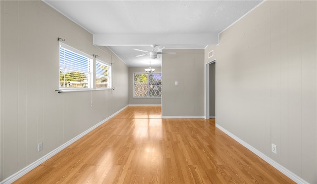 empty room featuring beam ceiling, wooden walls, ceiling fan with notable chandelier, and light hardwood / wood-style flooring