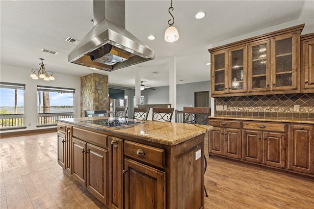 kitchen featuring island range hood, light wood-type flooring, black electric cooktop, and a kitchen breakfast bar