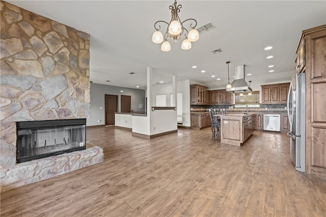 kitchen with appliances with stainless steel finishes, wood-type flooring, a center island, island exhaust hood, and pendant lighting