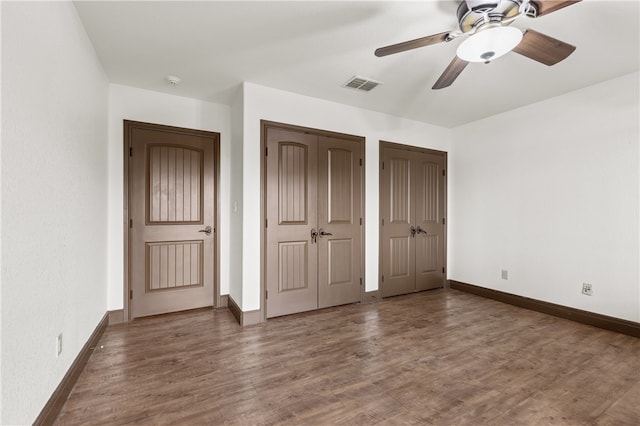 unfurnished bedroom with ceiling fan, dark hardwood / wood-style floors, and two closets