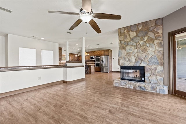 unfurnished living room with ceiling fan, hardwood / wood-style flooring, and a stone fireplace