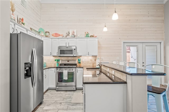 kitchen with appliances with stainless steel finishes, a kitchen bar, pendant lighting, wooden walls, and white cabinets