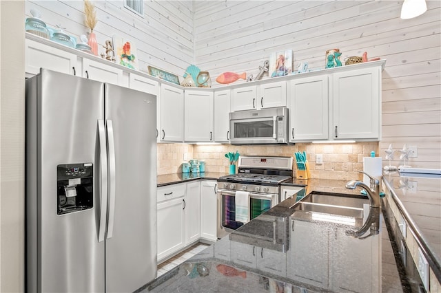 kitchen featuring stainless steel appliances, wood walls, tasteful backsplash, dark stone countertops, and white cabinets