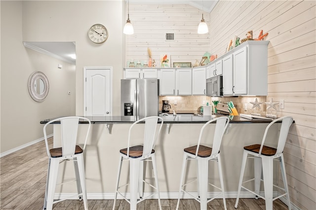 kitchen with stainless steel appliances, ornamental molding, decorative light fixtures, light hardwood / wood-style flooring, and white cabinets