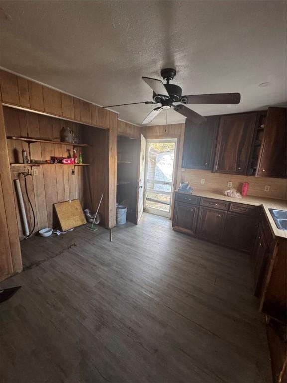 kitchen with wooden walls, wood finished floors, light countertops, dark brown cabinets, and a sink