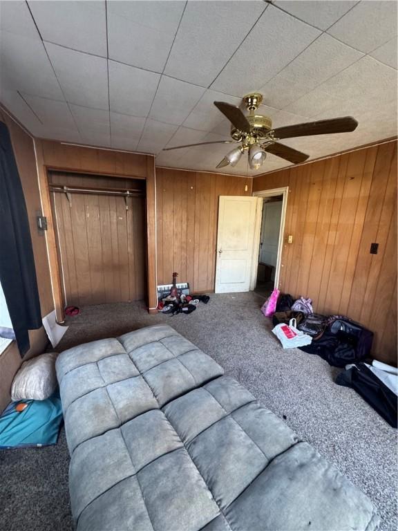 bedroom featuring a closet, carpet, a ceiling fan, and wooden walls