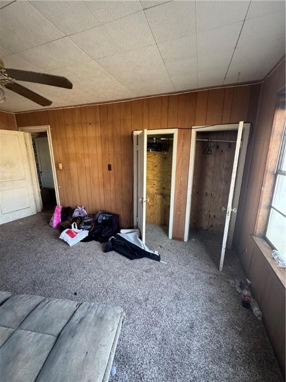 unfurnished bedroom featuring ceiling fan, carpet, wood walls, and two closets