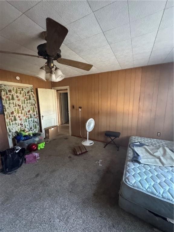 unfurnished bedroom with carpet floors, wood walls, and a ceiling fan