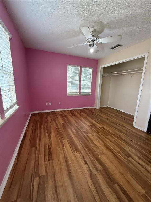 unfurnished bedroom featuring a closet, visible vents, a ceiling fan, a textured ceiling, and wood finished floors