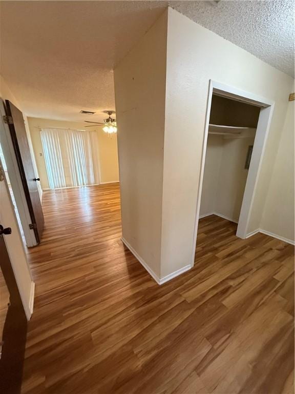 corridor featuring a textured ceiling, wood finished floors, and baseboards