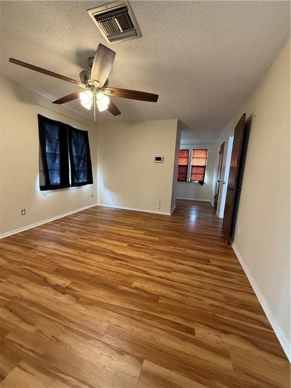 unfurnished room with a textured ceiling, wood finished floors, visible vents, and baseboards