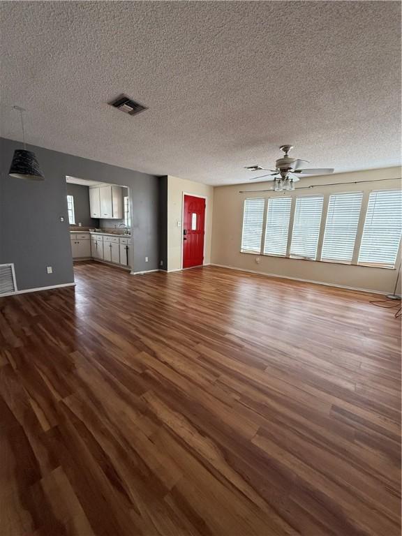 unfurnished living room with baseboards, dark wood-type flooring, visible vents, and a ceiling fan