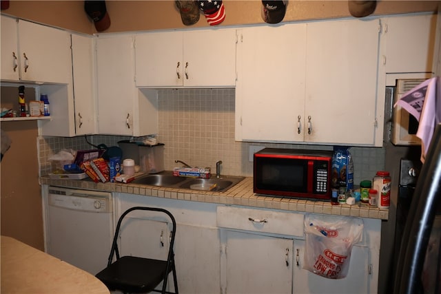 kitchen featuring tile countertops, white dishwasher, white cabinets, sink, and tasteful backsplash