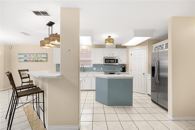 kitchen with a breakfast bar, backsplash, white cabinets, hanging light fixtures, and stainless steel appliances