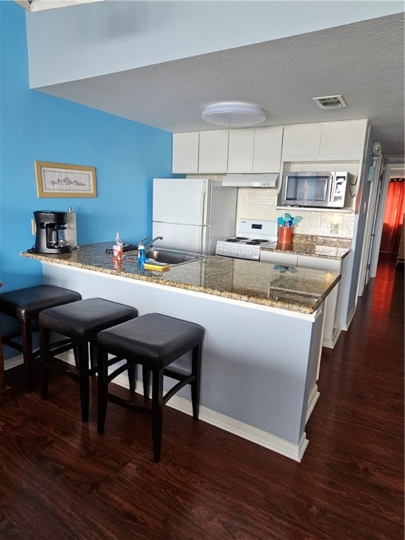 kitchen with white appliances, dark hardwood / wood-style floors, white cabinetry, and kitchen peninsula