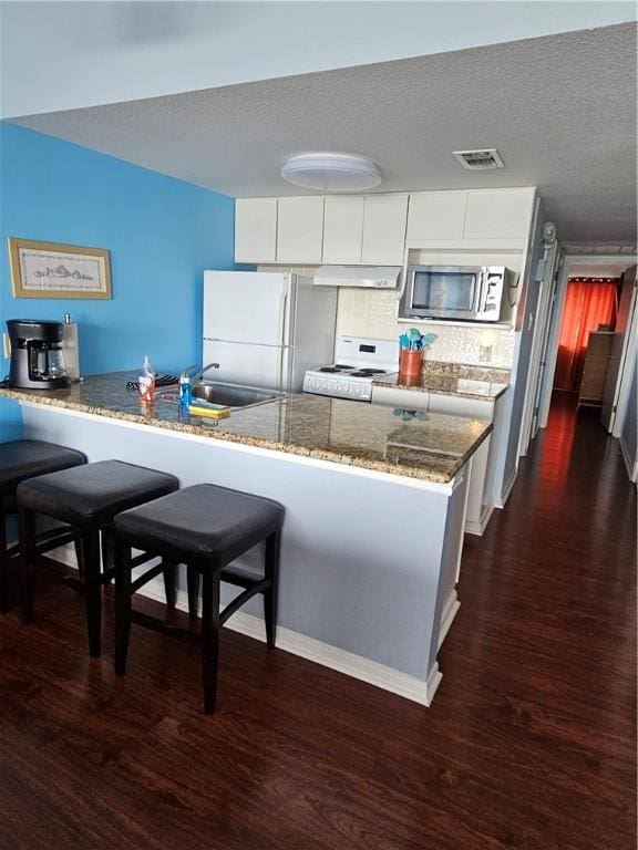 15425 Fortuna Bay Dr Unit 314, Corpus Christi, TX 78418 - kitchen featuring white appliances, under cabinet range hood, a sink, a breakfast bar area, and dark wood-style floors