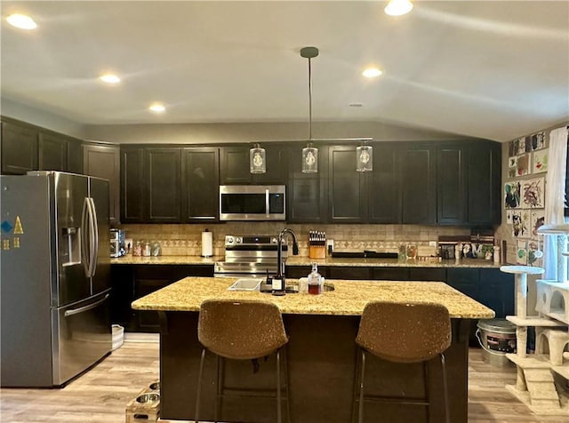 kitchen featuring appliances with stainless steel finishes, pendant lighting, an island with sink, light stone countertops, and light wood-type flooring