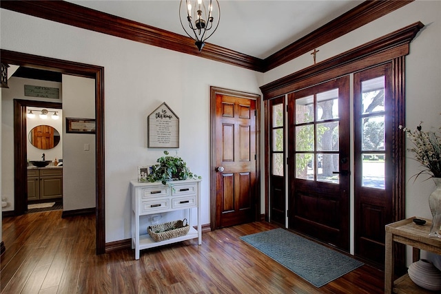 entrance foyer with baseboards, dark wood-type flooring, a notable chandelier, and crown molding