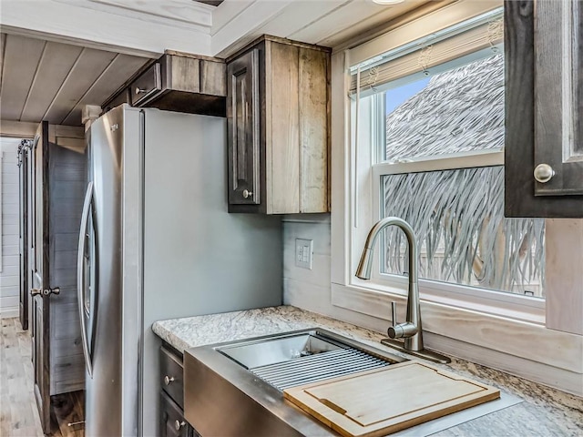 kitchen with dark brown cabinets, a sink, freestanding refrigerator, and light wood-style floors