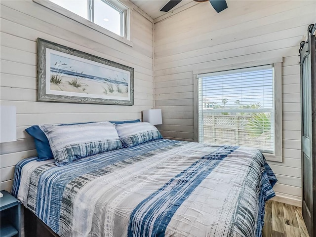 bedroom featuring a ceiling fan, wood walls, and wood finished floors