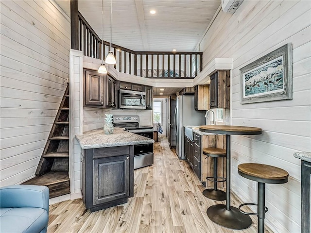 kitchen featuring light wood-style flooring, wooden walls, appliances with stainless steel finishes, and decorative light fixtures