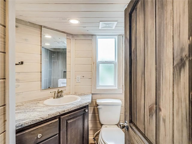 bathroom featuring visible vents, wooden walls, toilet, and vanity