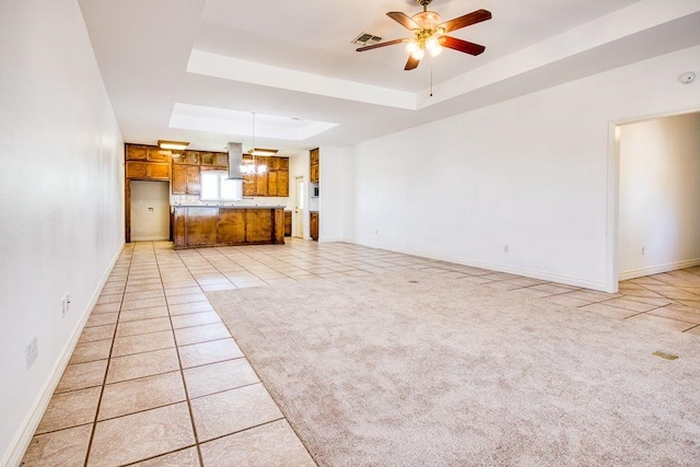 unfurnished living room with visible vents, light tile patterned floors, baseboards, ceiling fan, and a tray ceiling