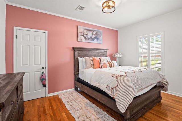 bedroom featuring baseboards, visible vents, ornamental molding, and wood finished floors