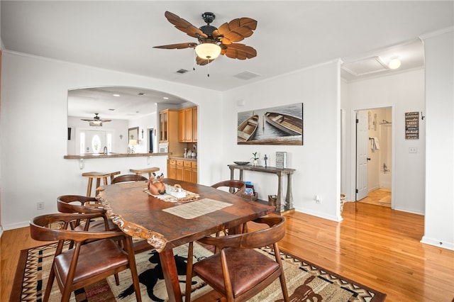 dining space with ceiling fan, visible vents, arched walkways, baseboards, and light wood finished floors