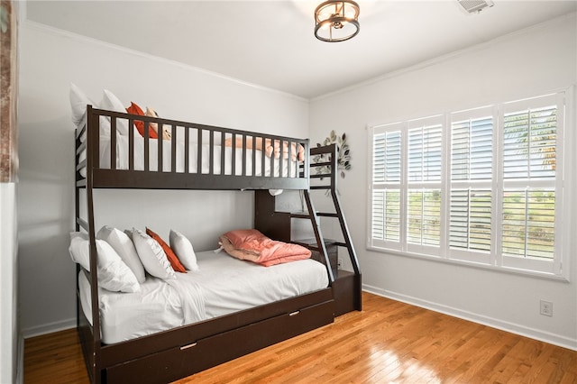 bedroom with baseboards, visible vents, ornamental molding, and wood finished floors