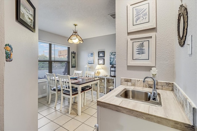 kitchen featuring decorative light fixtures, sink, light tile patterned flooring, and a textured ceiling