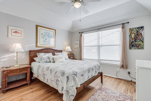 bedroom with a textured ceiling, vaulted ceiling, ceiling fan, and light hardwood / wood-style flooring