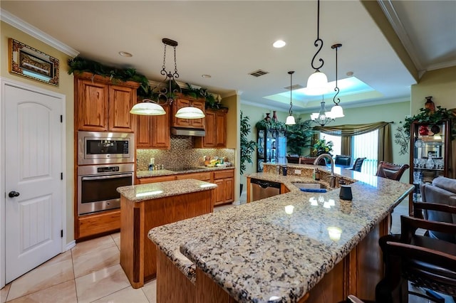 kitchen featuring appliances with stainless steel finishes, tasteful backsplash, decorative light fixtures, a large island with sink, and sink