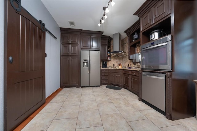 kitchen featuring wall chimney range hood, dark brown cabinets, stainless steel appliances, and a barn door