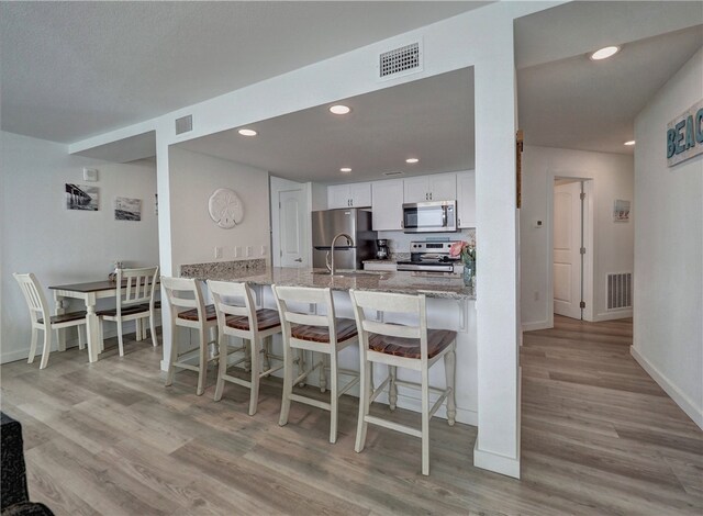 kitchen featuring stainless steel appliances, kitchen peninsula, light stone countertops, white cabinetry, and light hardwood / wood-style flooring