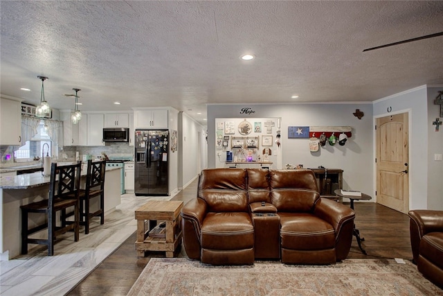 living room featuring a textured ceiling, sink, light wood-type flooring, and crown molding