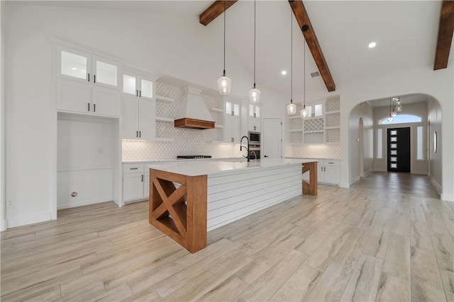 kitchen with stainless steel microwave, hanging light fixtures, a kitchen island with sink, beam ceiling, and white cabinets