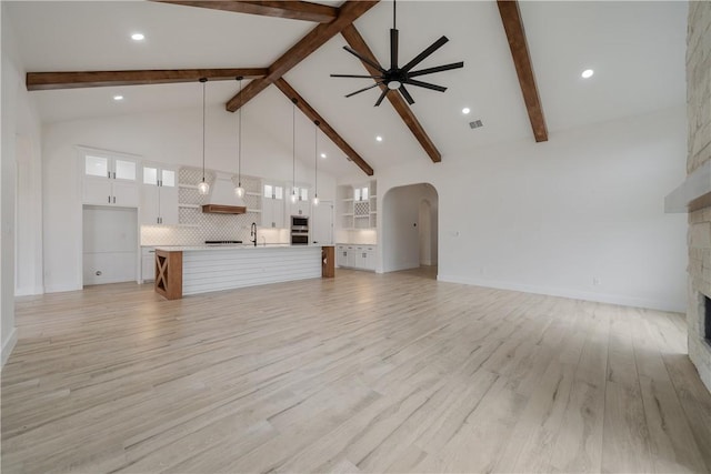 unfurnished living room with a stone fireplace, light wood-type flooring, ceiling fan, high vaulted ceiling, and sink